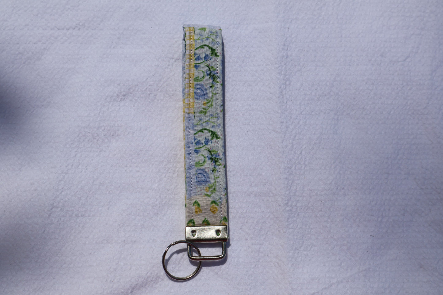 Fabric key fob with a patchwork yellow and blue floral pattern and a Mia grace brand label and a key ring