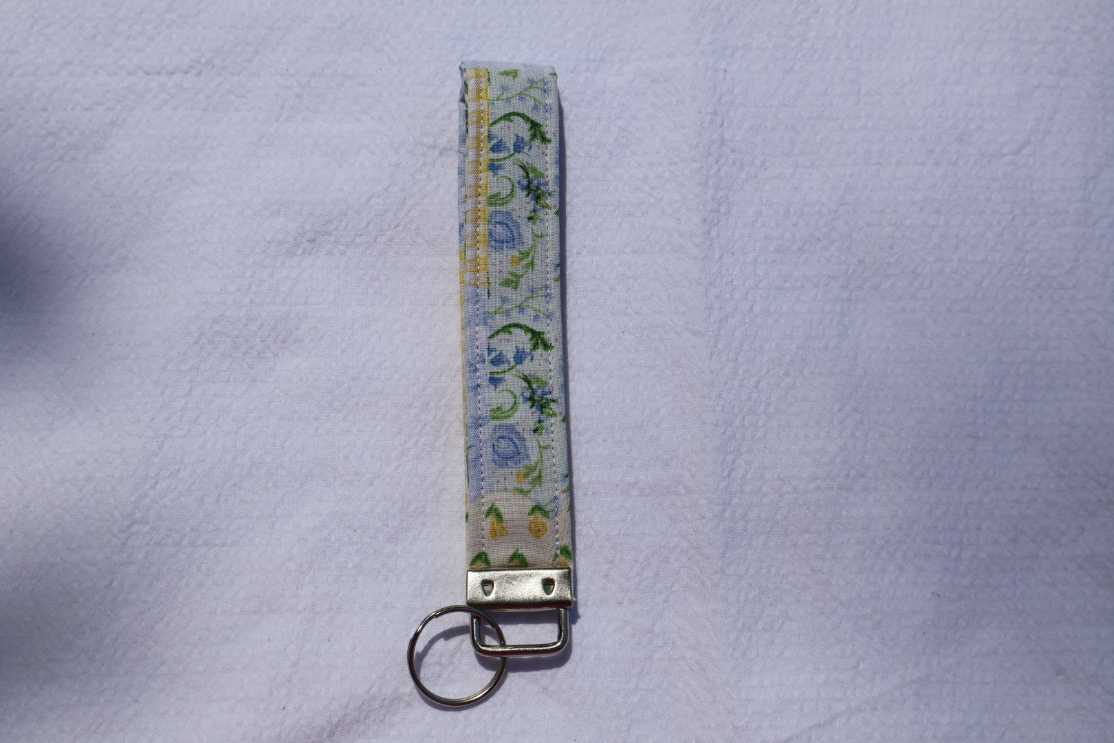 Fabric key fob with a patchwork yellow and blue floral pattern and a Mia grace brand label and a key ring