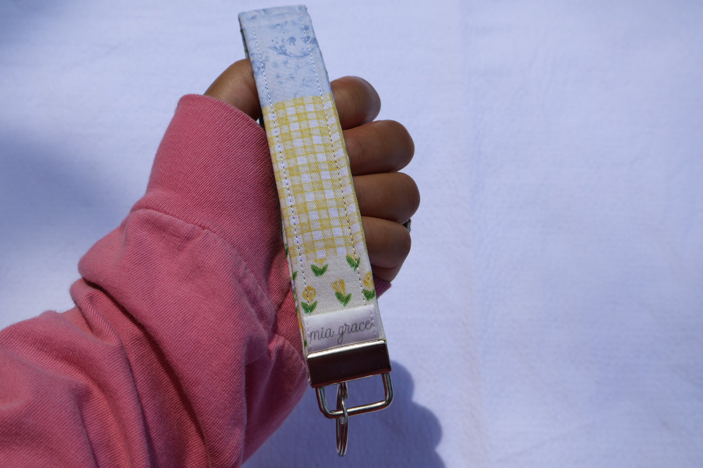 close up of a Fabric key fob with a patchwork yellow and blue floral pattern and a Mia grace brand label and a key ring