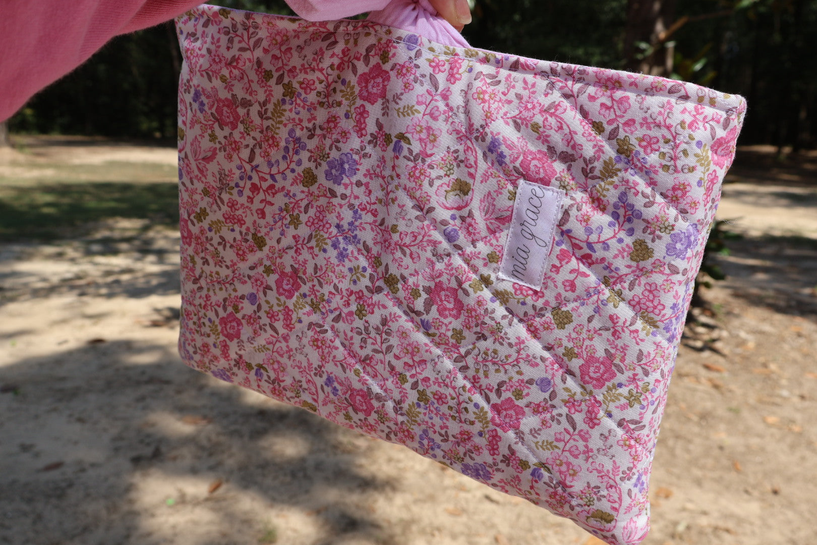 close up of a pink and purple  Floral-patterned fabric with a pink bow tie closure and a Mia grace brand label