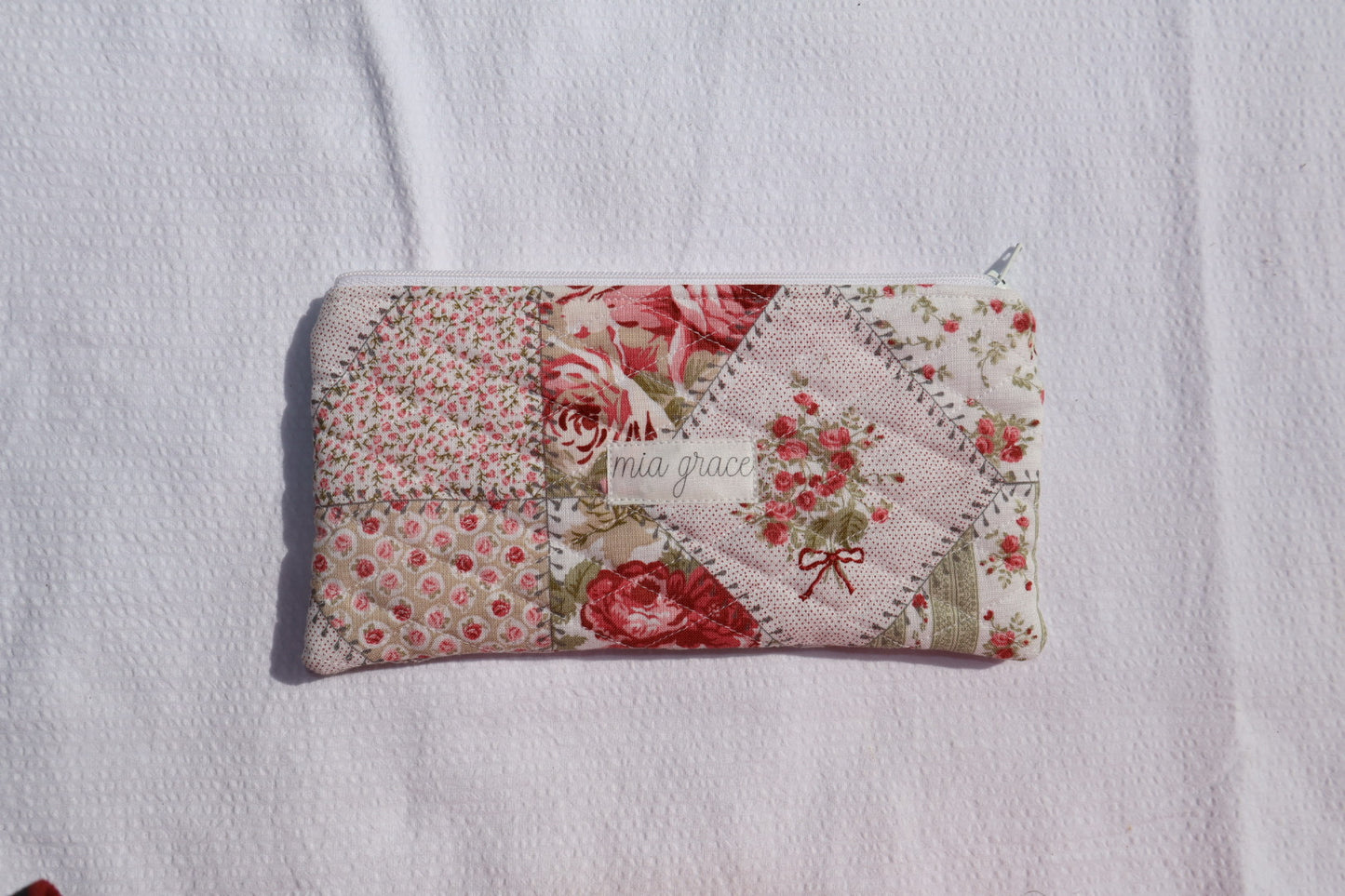 Floral patchwork patterned pouch with 'mia grace' branding label with a zipper closure