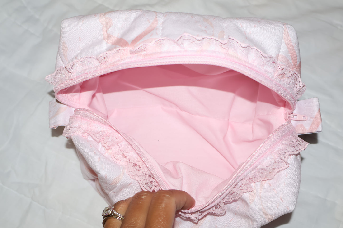 soft pink with pink bows quilted boxy pouch with a Mia Grace brand label and a white zipper and pull tabs. zipper has a pink lace trim. soft pink inner fabric
