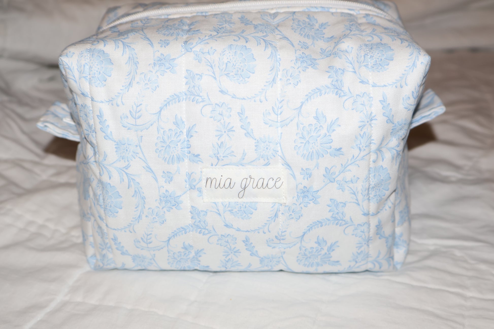 soft blue floral paisley quilted boxy pouch with a Mia Grace brand label and a white zipper and pull tabs.