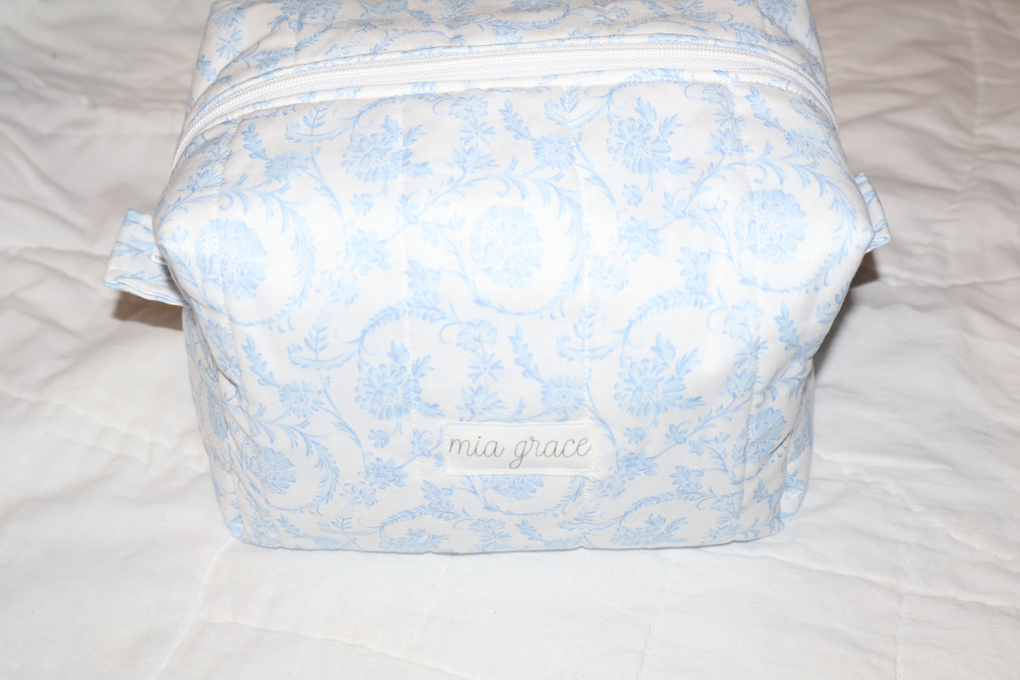 soft blue floral paisley quilted boxy pouch with a Mia Grace brand label and a white zipper and pull tabs.