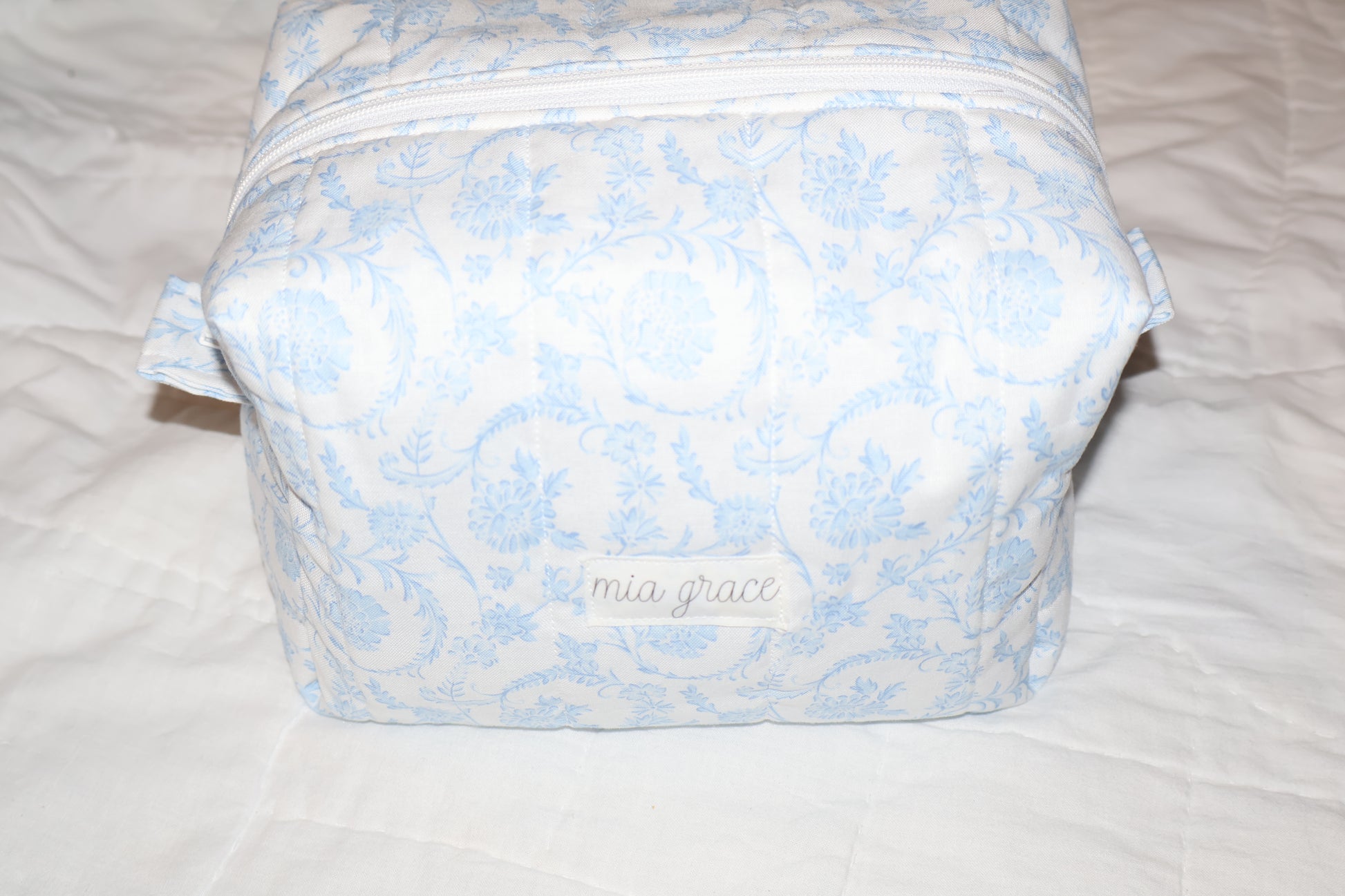 soft blue floral paisley quilted boxy pouch with a Mia Grace brand label and a white zipper and pull tabs.