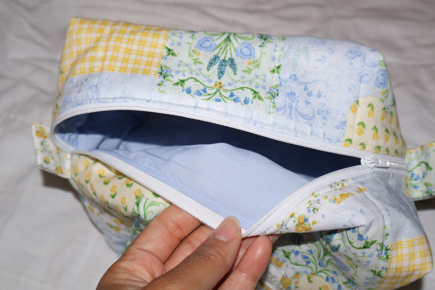 yellow, blue, and green  floral-patchwork quilted boxy pouch with a Mia Grace brand label and a white zipper and pull tabs. Blue inner fabric