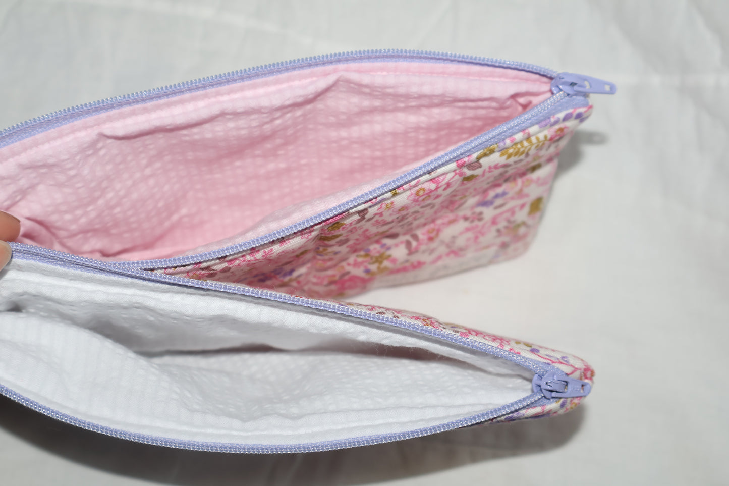 close up of pencil pouch's inner fabric. one has a pink inner fabric and one has a white inner  fabric. 