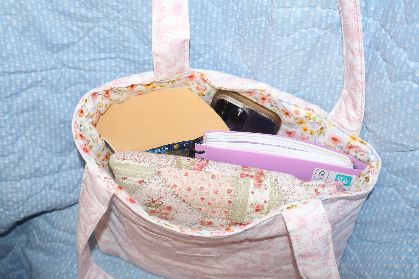 Tote bag with thick paperback book, cellphone, small writing tablet, and a bible inside. 