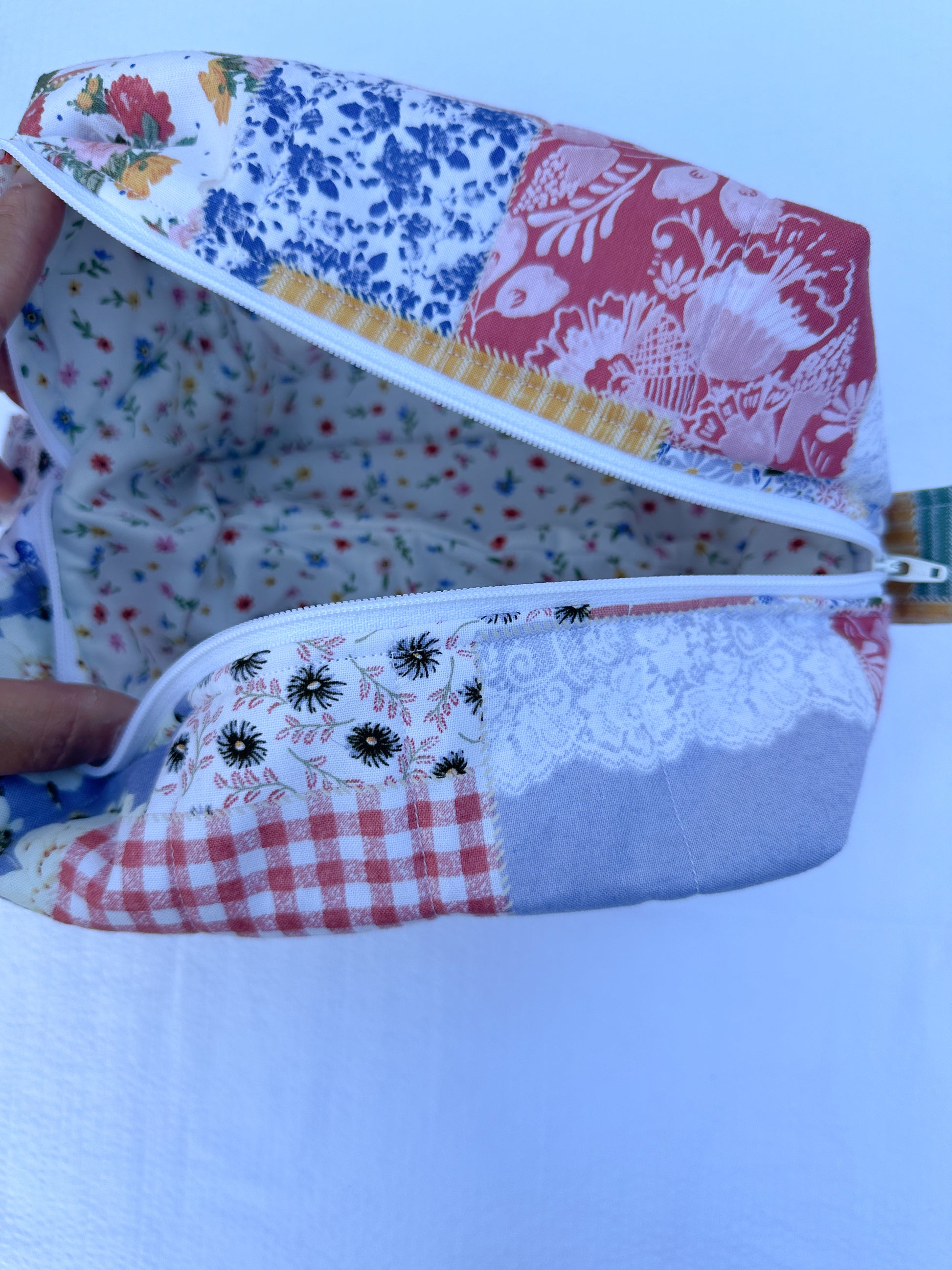 Patchwork-style fabric quilted boxy pouch with floral and gingham  patterns with a Mia grace brand label and white zipper  and pull tabs. ditsy wildflowers floral inner fabric