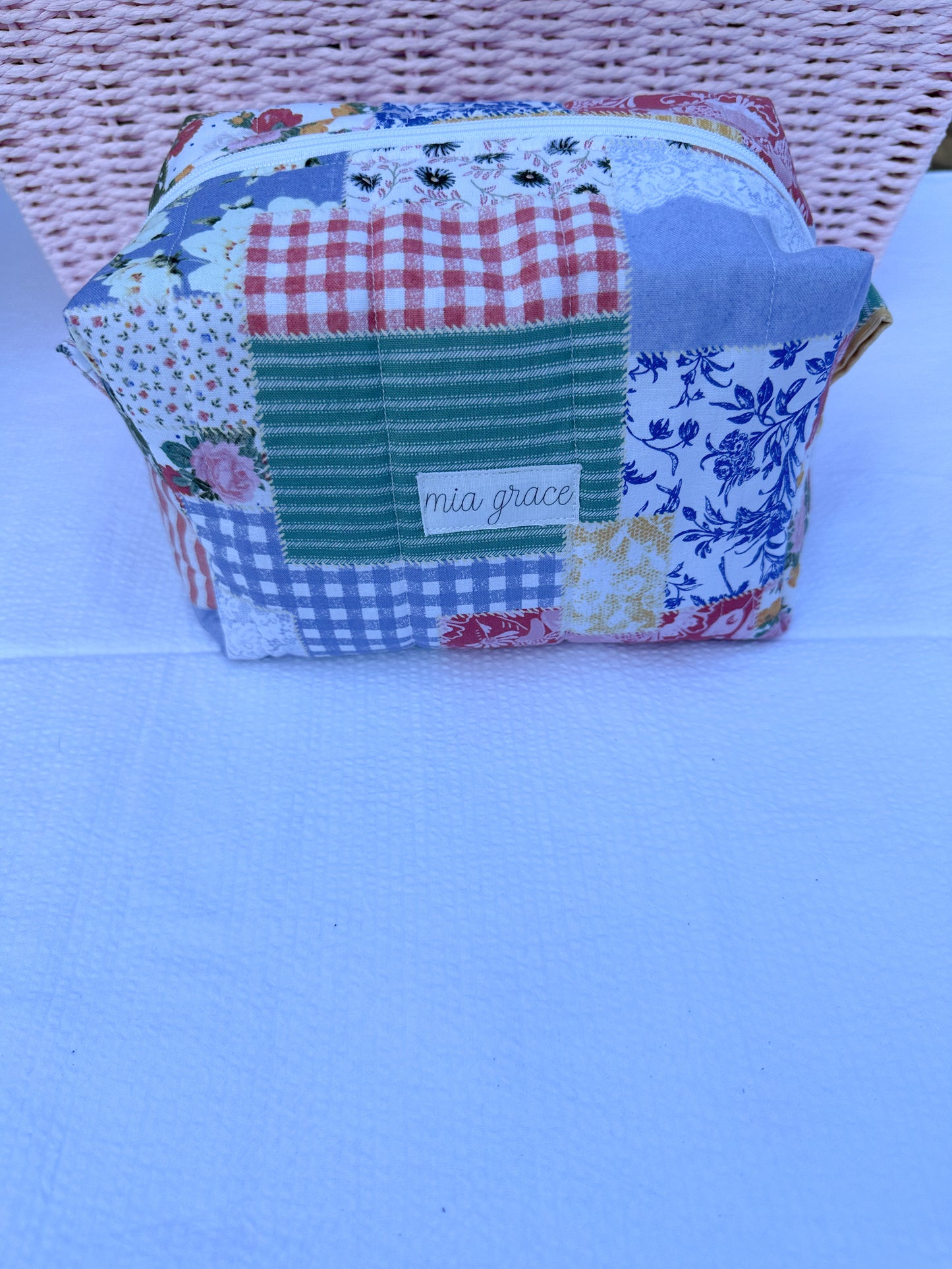Patchwork-style fabric quilted boxy pouch with floral and gingham  patterns with a Mia grace brand label and white zipper  and pull tabs. 