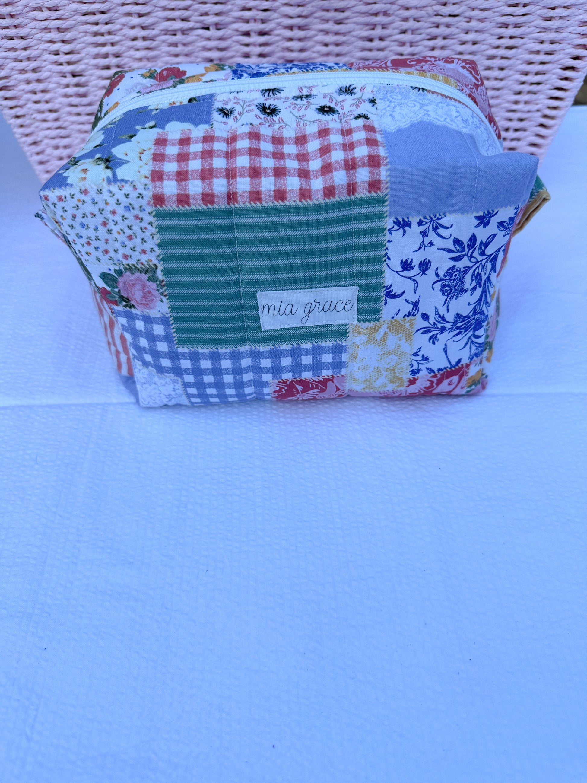 Patchwork-style fabric quilted boxy pouch with floral and gingham  patterns with a Mia grace brand label and white zipper  and pull tabs. 