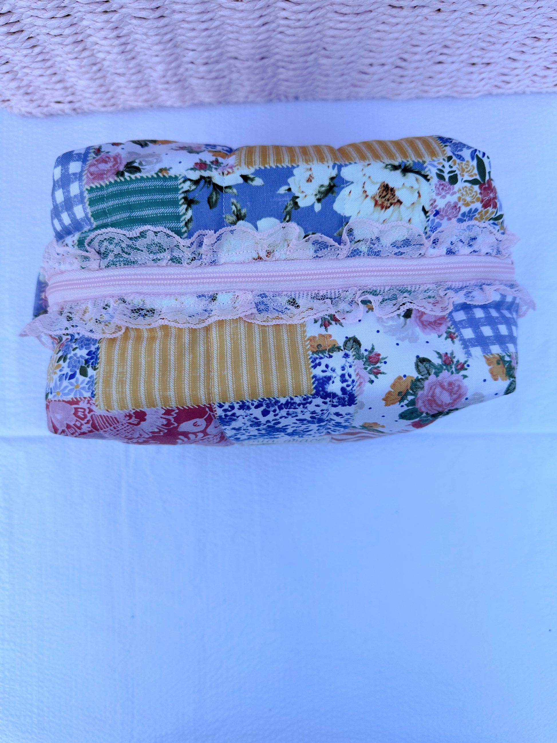 Patchwork-style fabric quilted boxy pouch with floral and gingham  patterns with a Mia grace brand label and pink zipper with pink lace trim and pull tabs.