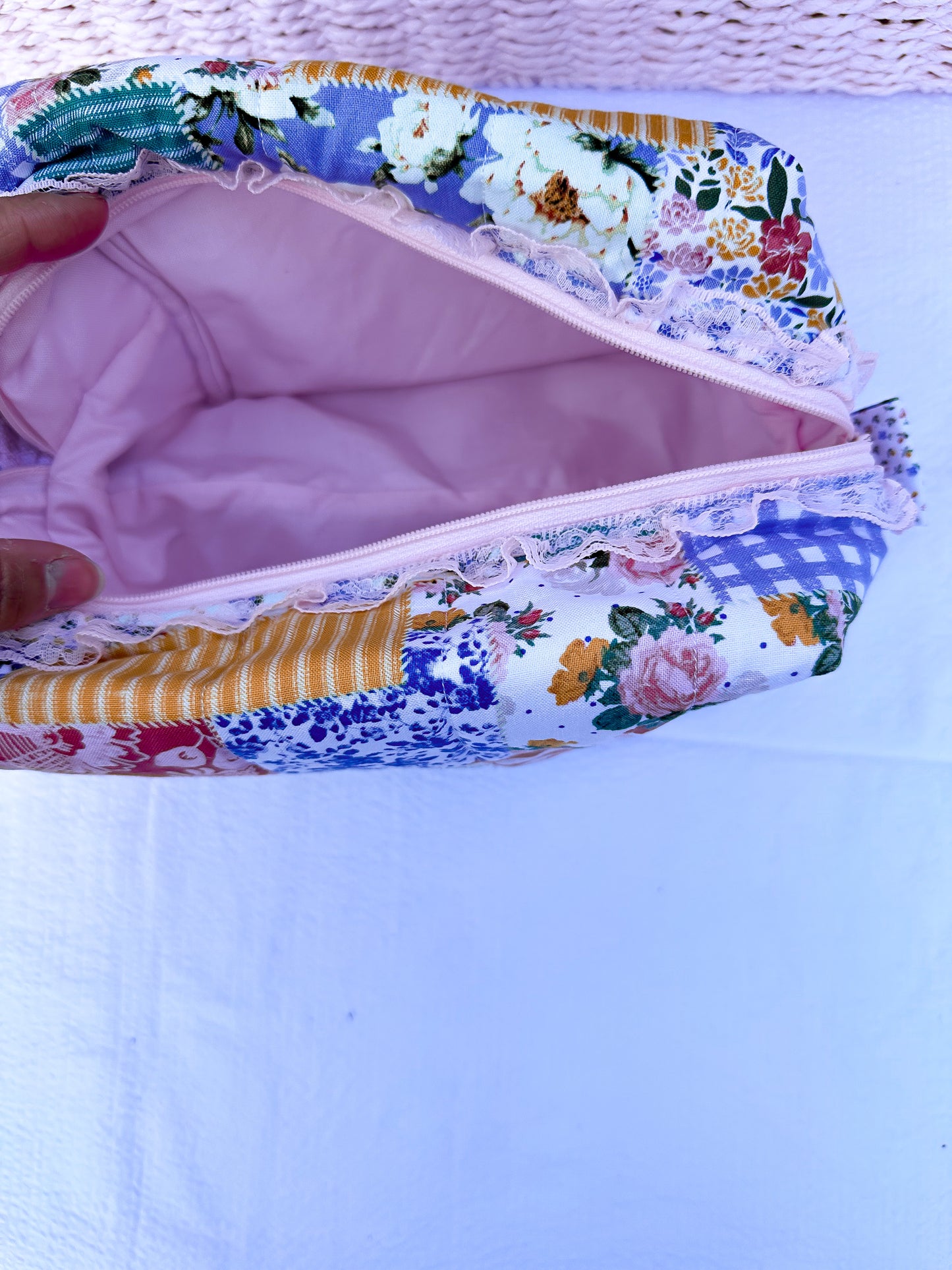 Patchwork-style fabric quilted boxy pouch with floral and gingham  patterns with a Mia grace brand label and pink zipper with pink lace trim and pull tabs. soft pink inner fabric