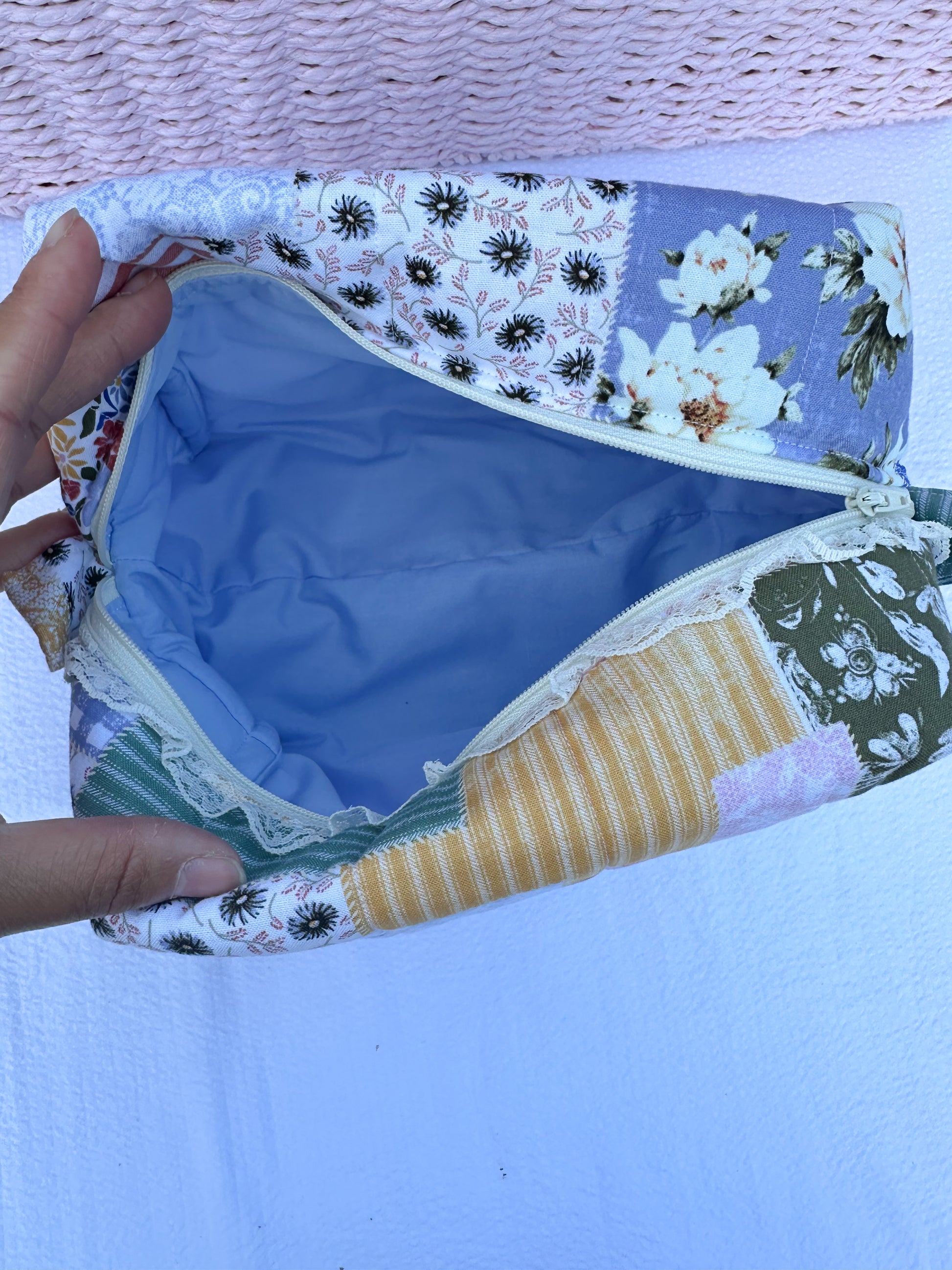 Patchwork-style fabric quilted boxy pouch with floral and gingham  patterns with a Mia grace brand label and cream zipper with cream one sided lace trim and pull tabs. Blue inner fabric