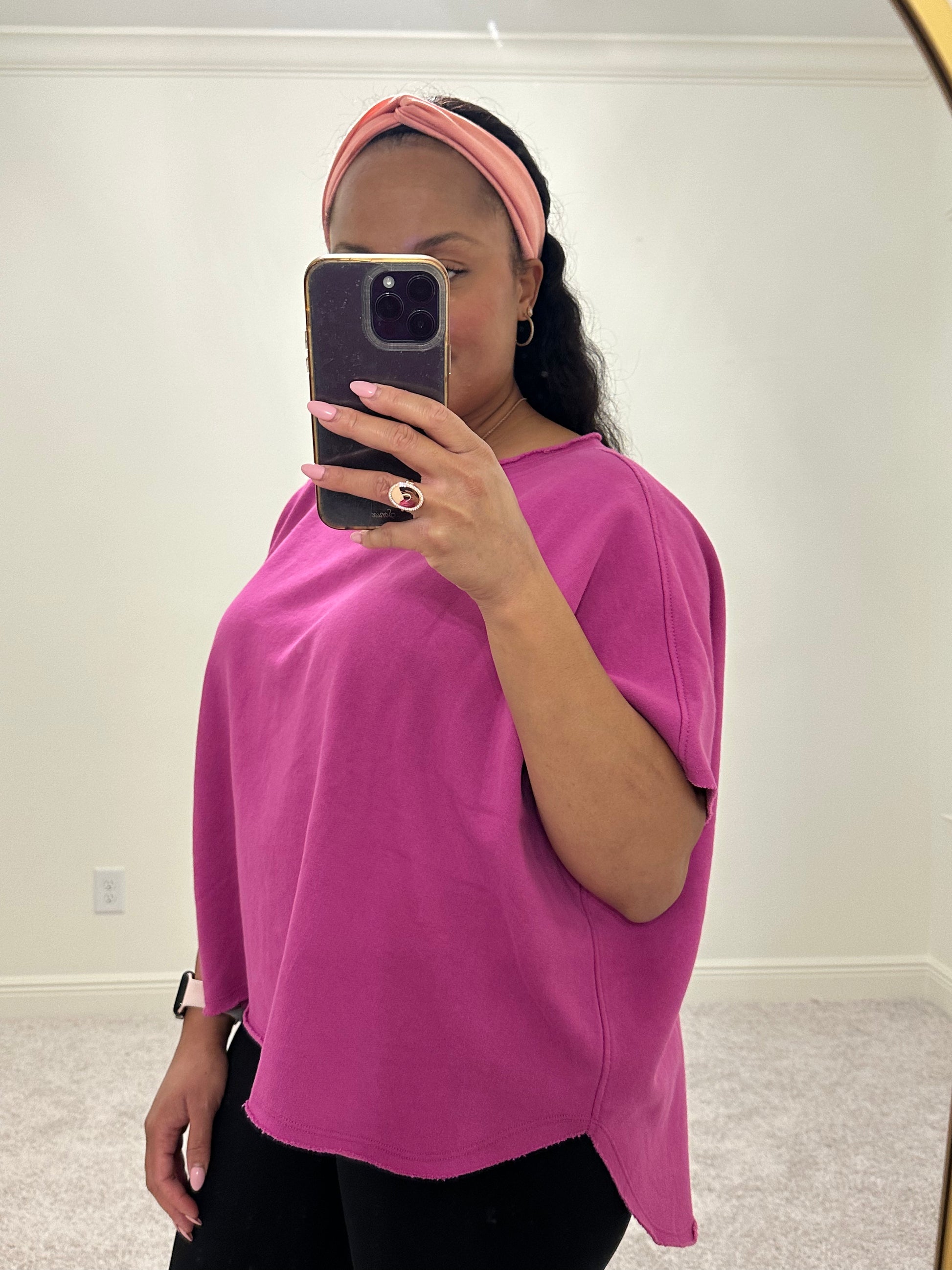 woman wearing an orchid color short sleeve dolman sleeve top that has a slight boatneck neckline and a hi-lo raw hem. 