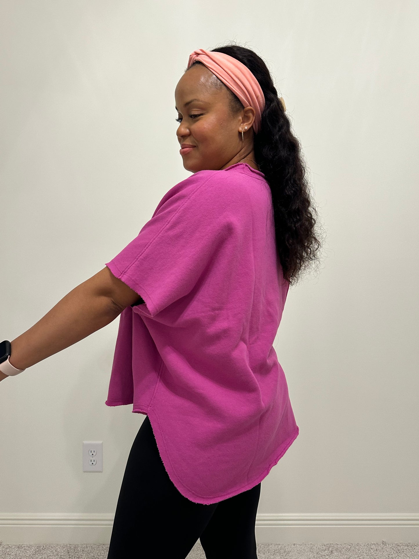 woman wearing an orchid color short sleeve dolman sleeve top that has a slight boatneck neckline and a hi-lo raw hem. 