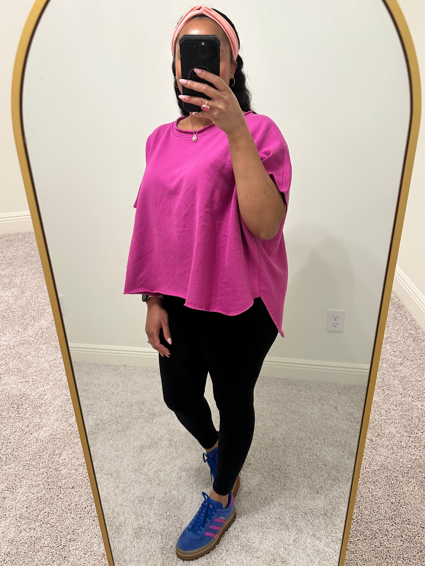 woman wearing an orchid color short sleeve dolman sleeve top that has a slight boatneck neckline and a hi-lo raw hem. 