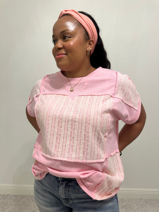 Person wearing a pink shirt with white lace patchwork detailing that is a relaxed fit. 