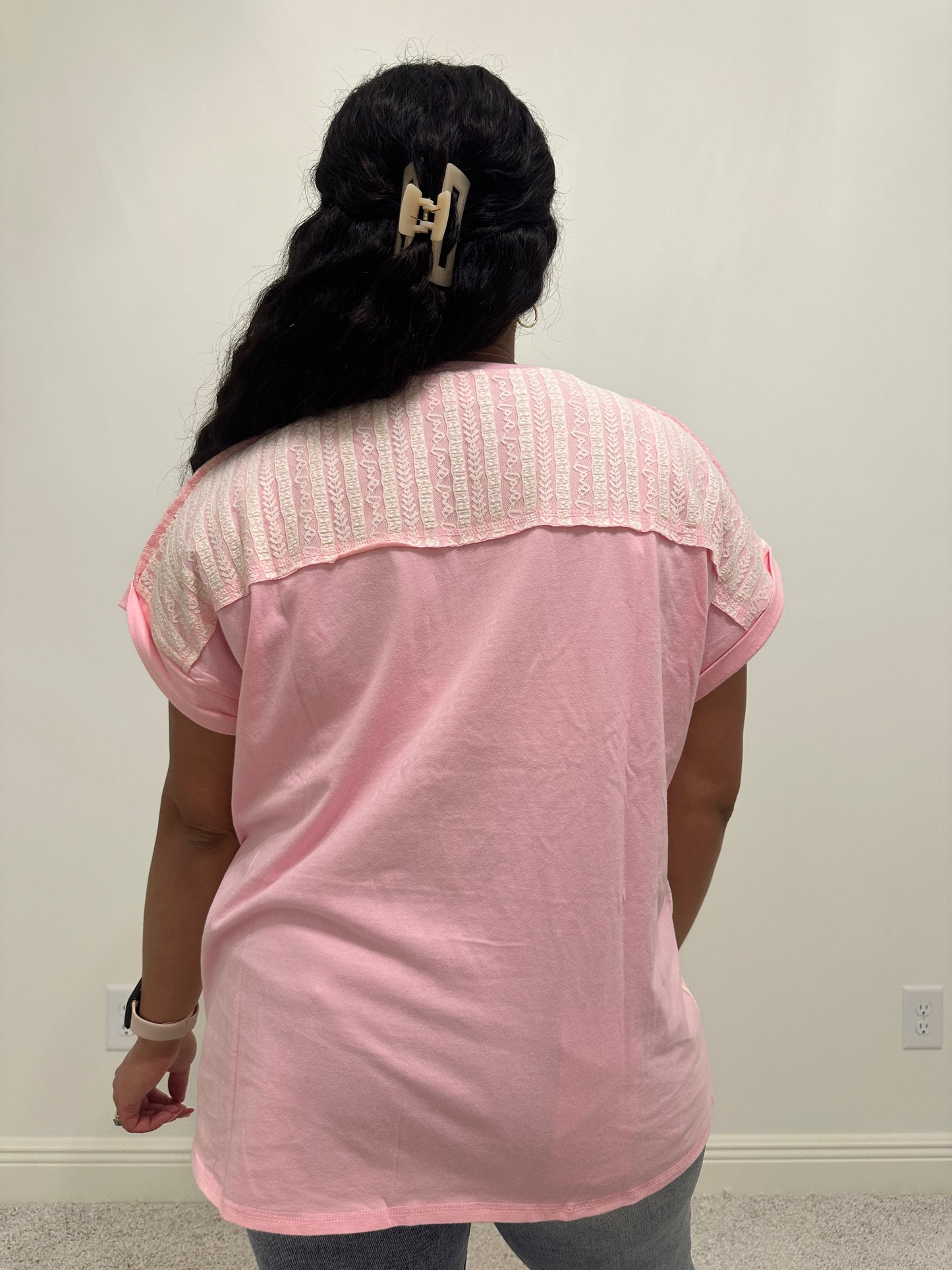 Person wearing a pink shirt with white lace patchwork detailing that is a relaxed fit. 