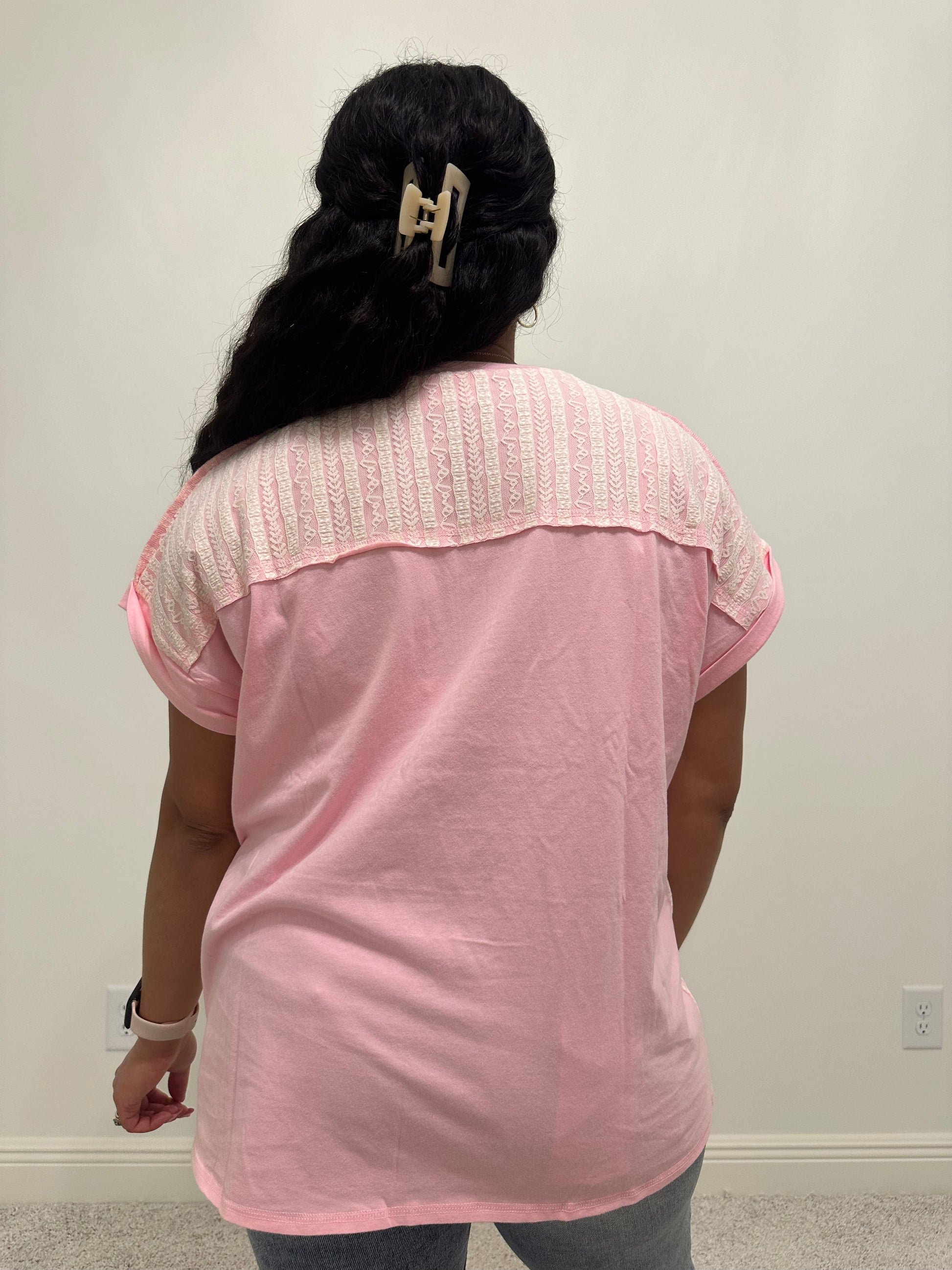 Person wearing a pink shirt with white lace patchwork detailing that is a relaxed fit. 