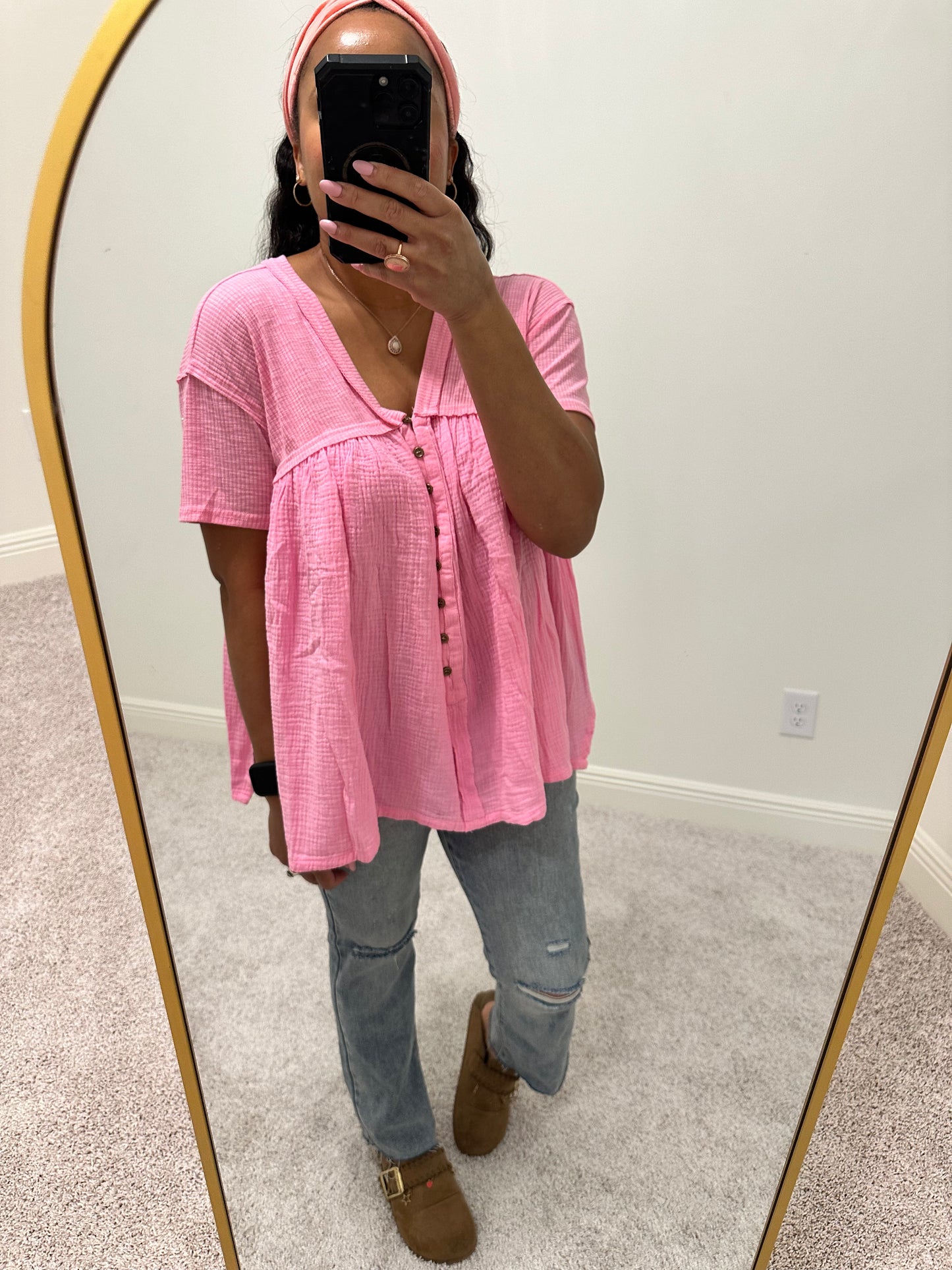 Person wearing a pink shirt that is a loose flowy babydoll style with buttons 2/3 down the front of the shirt with a side slit.