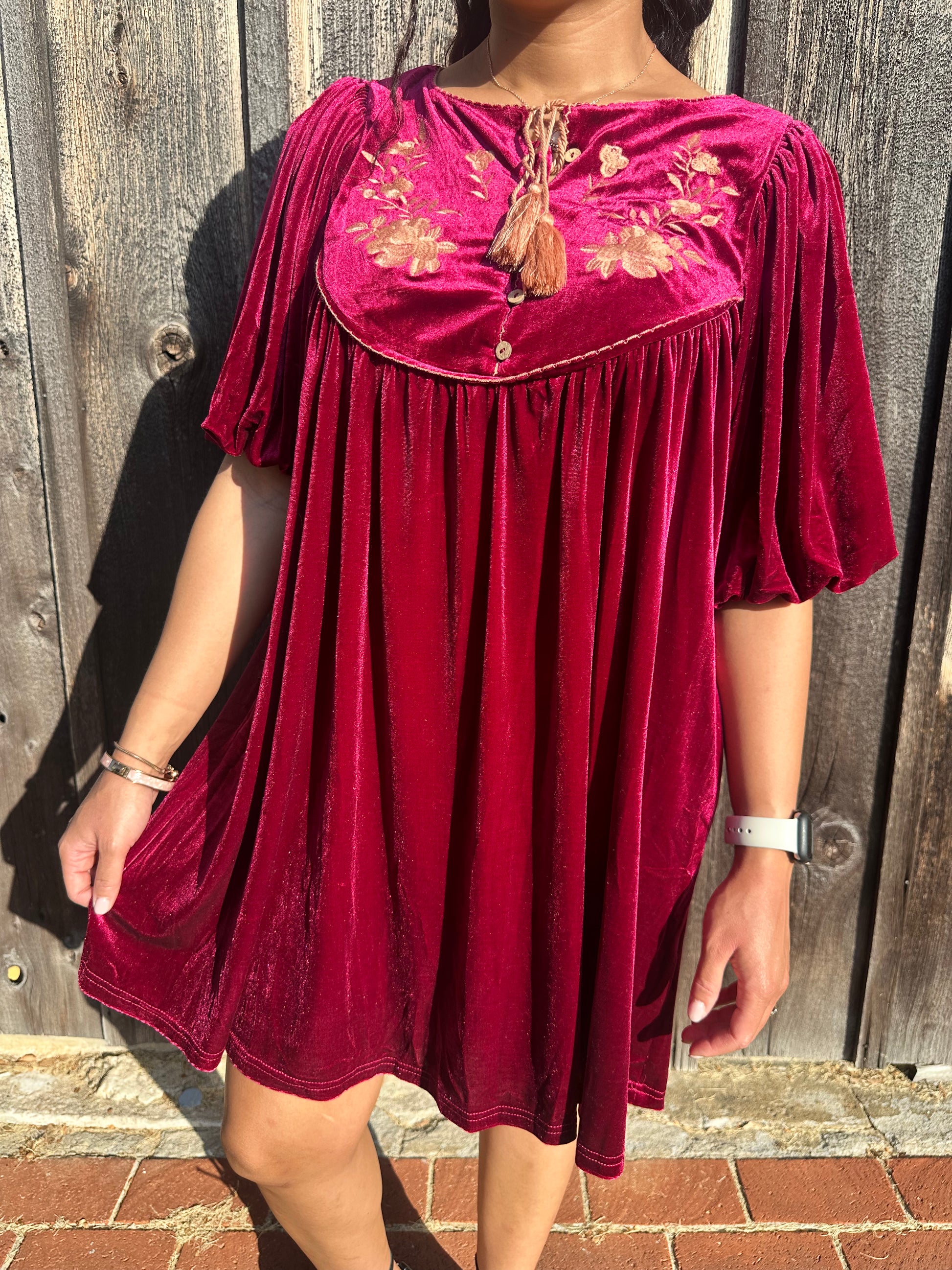 Maroon Dress with pleated detailing and scallop stitching details with floral embroidery on yoke and functional buttons with a tie tassel. Back paneling also has the floral embroidery detailing. The dress is short sleeve with flowy balloon sleeves. 