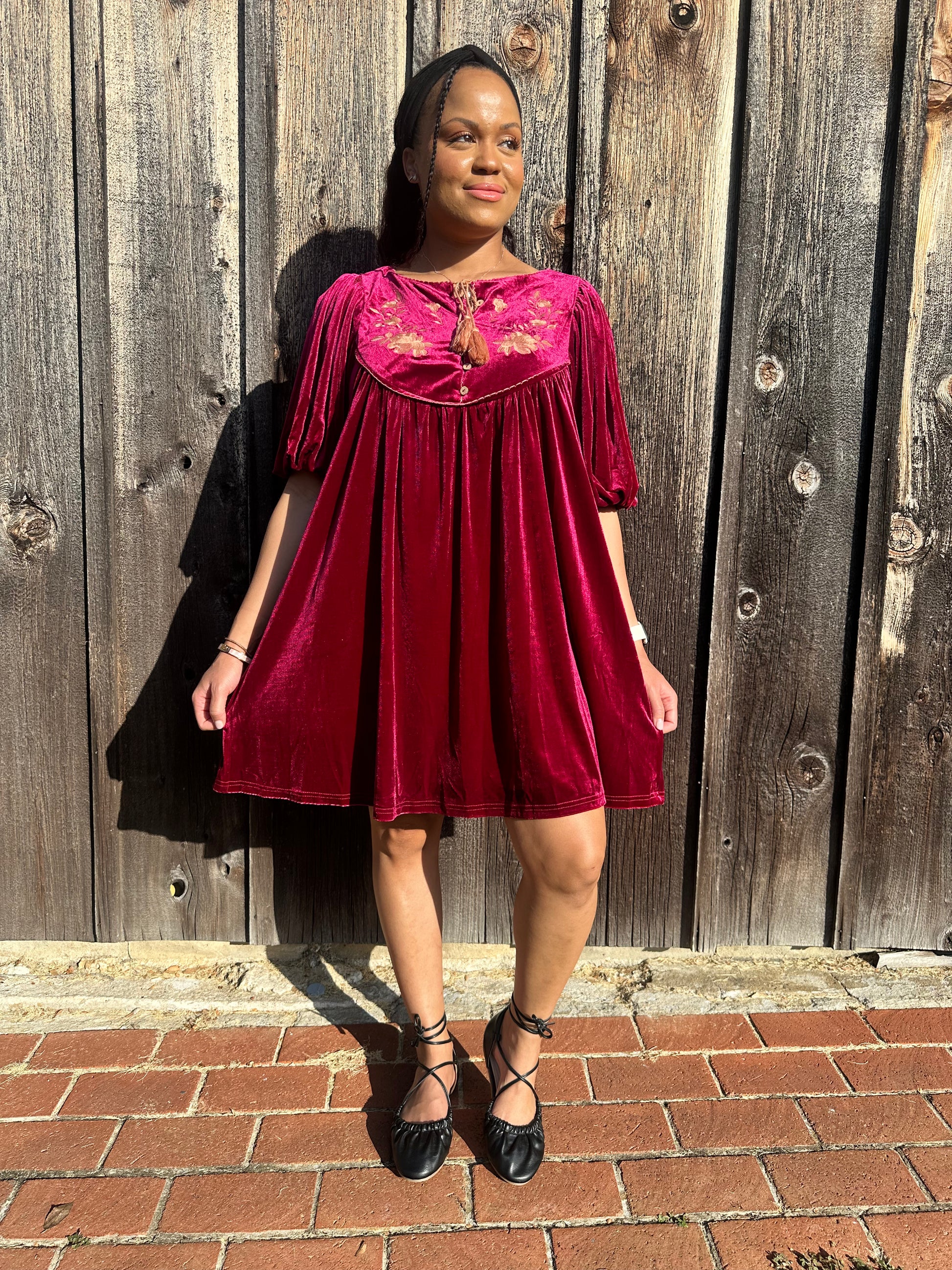 Maroon Dress with pleated detailing and scallop stitching details with floral embroidery on yoke and functional buttons with a tie tassel. Back paneling also has the floral embroidery detailing. The dress is short sleeve with flowy balloon sleeves. 