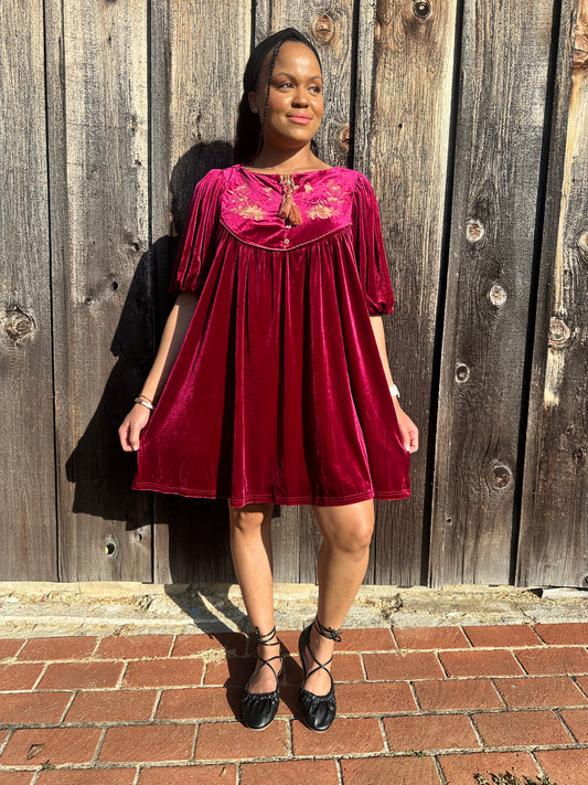Maroon Dress with pleated detailing and scallop stitching details with floral embroidery on yoke and functional buttons with a tie tassel. Back paneling also has the floral embroidery detailing. The dress is short sleeve with flowy balloon sleeves. 